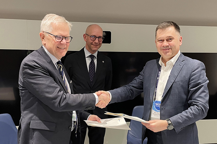 Handskakning mellan två leende män i kostym. En till man bakom.